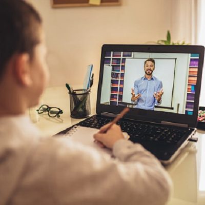 Niño tomando apuntes mientras sigue una clase por videoconferencia en su ordenador.