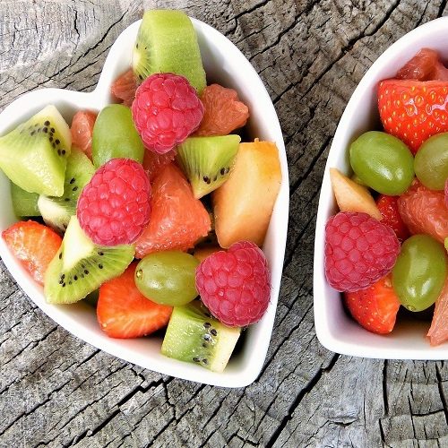 Ensaladas de frutas en tazones con forma de corazón, mezclando fresas, kiwis y uvas.